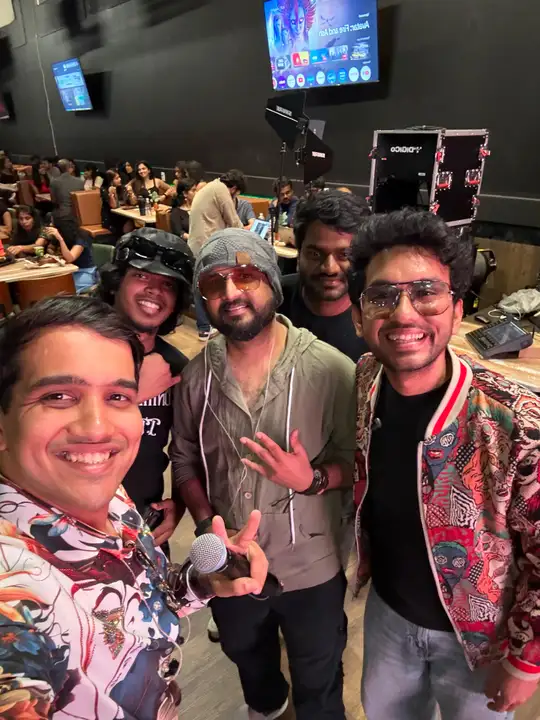 Band members and crew smiling in a selfie at the Dallas venue, mic in hand.